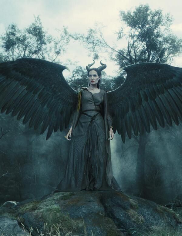 a woman with large black wings standing on top of a rock