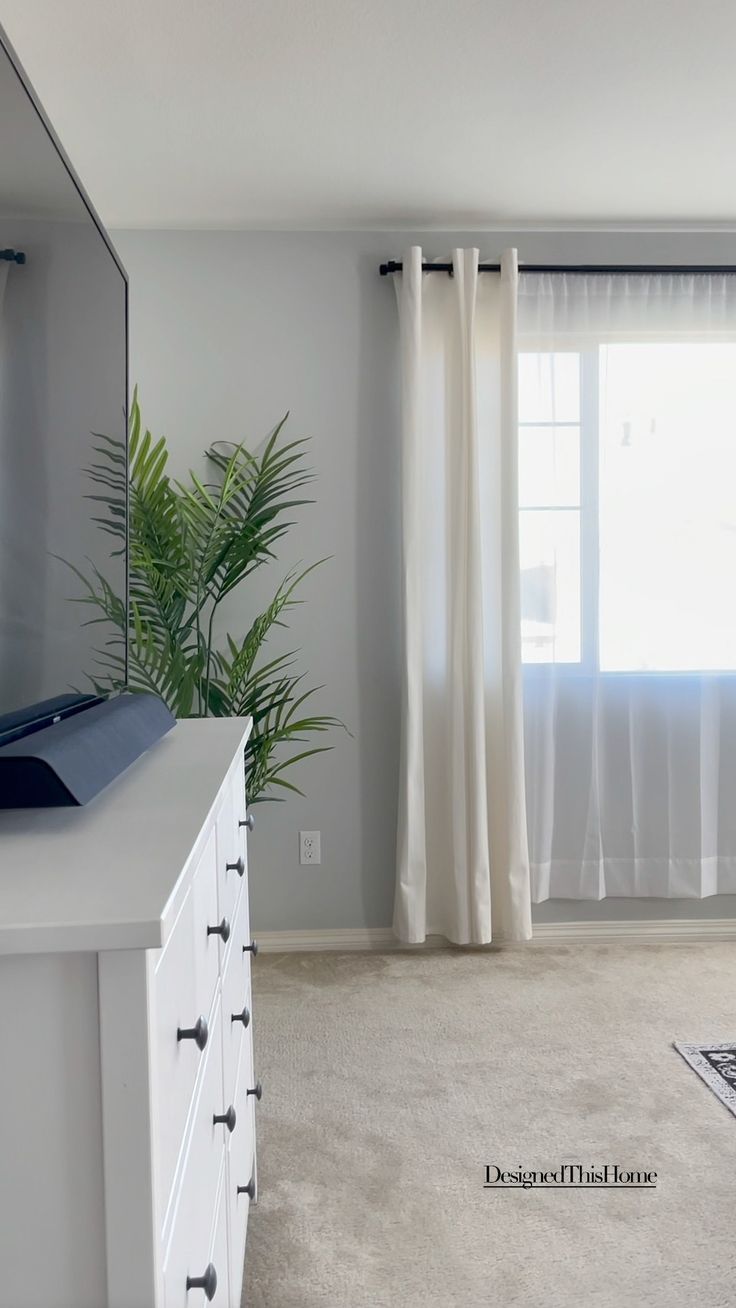 a white dresser sitting in front of a window next to a curtained window sill