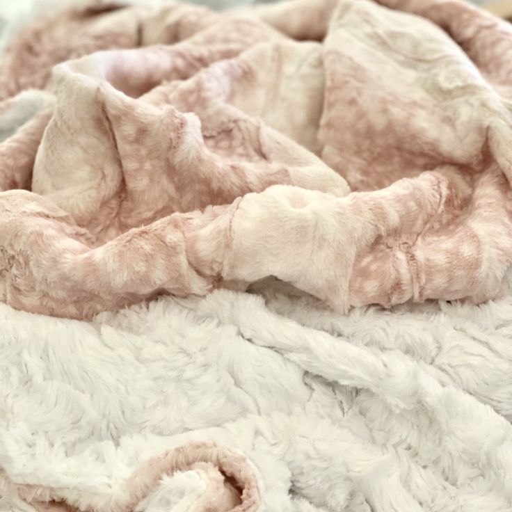 a blanket that is laying on top of a bed with pink and white fur covering it