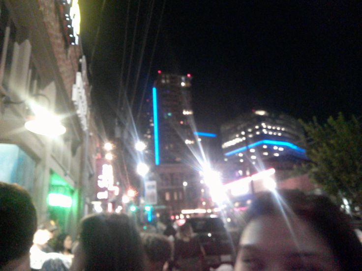 a group of people standing on the side of a street next to tall buildings at night