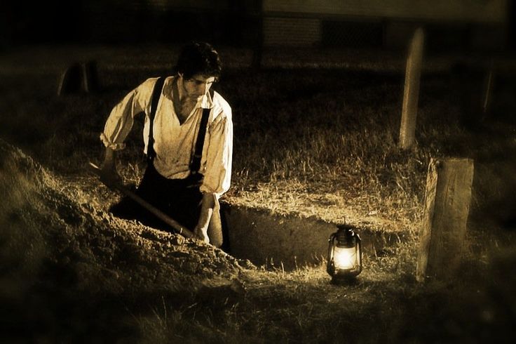 a man standing next to a lantern in the grass