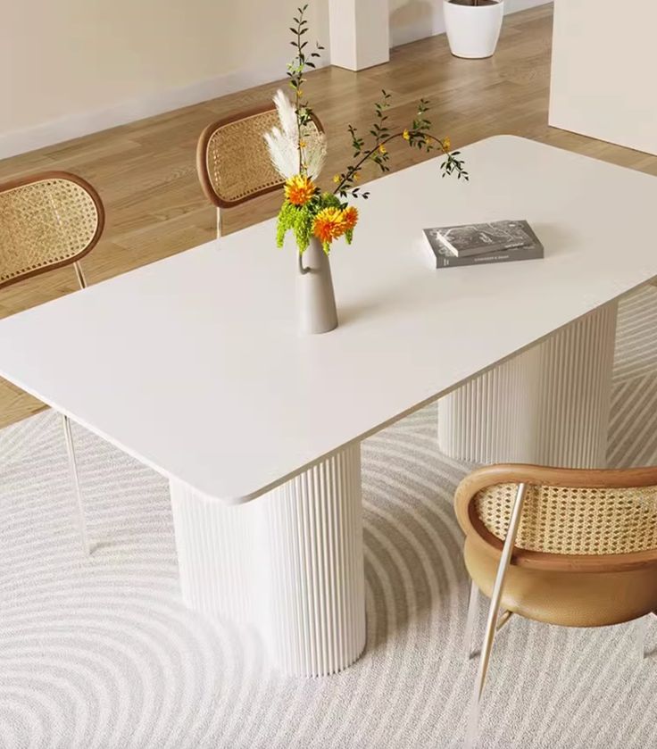 a white table with two chairs and a vase filled with flowers on top of it