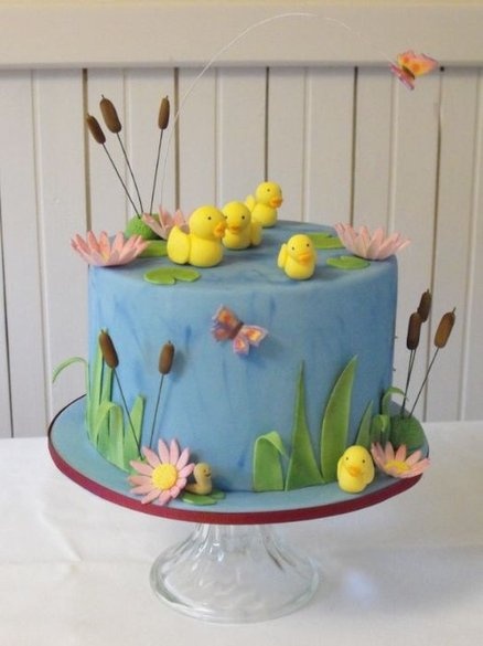 a blue cake decorated with yellow ducks and water lillies on a table in front of a white wall