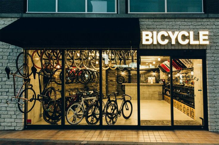 the bicycle shop has many bikes in it's display window and is lit up at night