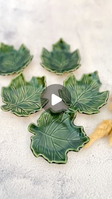 four green leaf shaped dishes sitting on top of a white countertop next to yarn