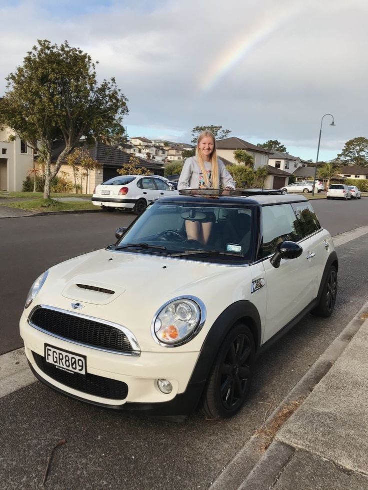 a woman sitting on top of a white mini cooper parked in front of a house