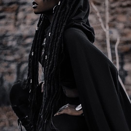 a woman with dreadlocks standing in front of a stone wall