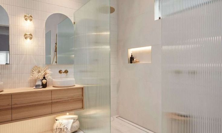 a white bathroom with two sinks and a shower stall next to the bathtub is illuminated by recessed lights