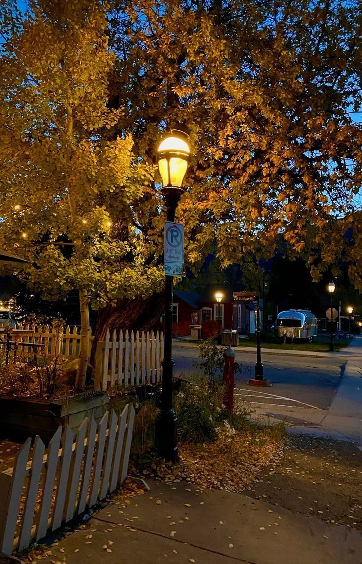 a street light sitting on the side of a road next to a white picket fence