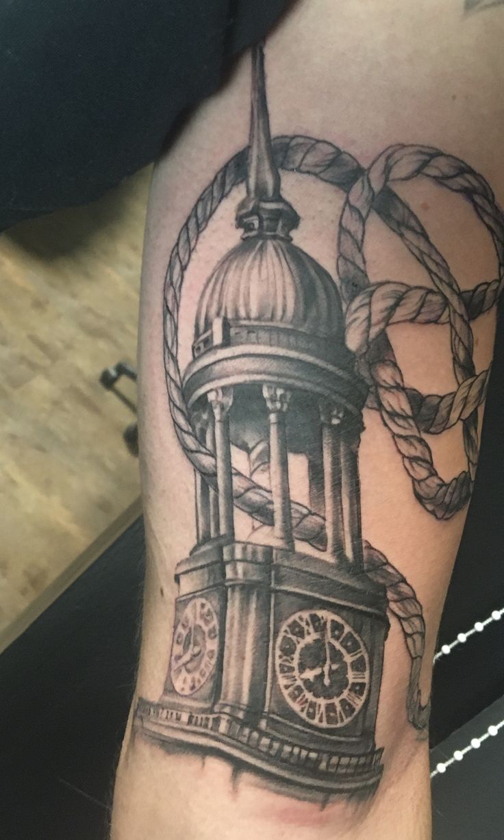 a black and white photo of a clock tower on someone's arm with rope around it