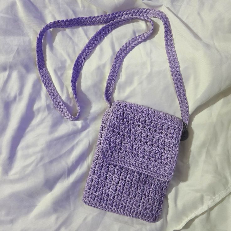 a purple crocheted purse sitting on top of a white bed covered in sheets