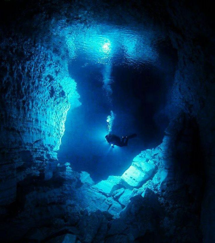 a man swimming in the water inside of a cave with blue light coming from it