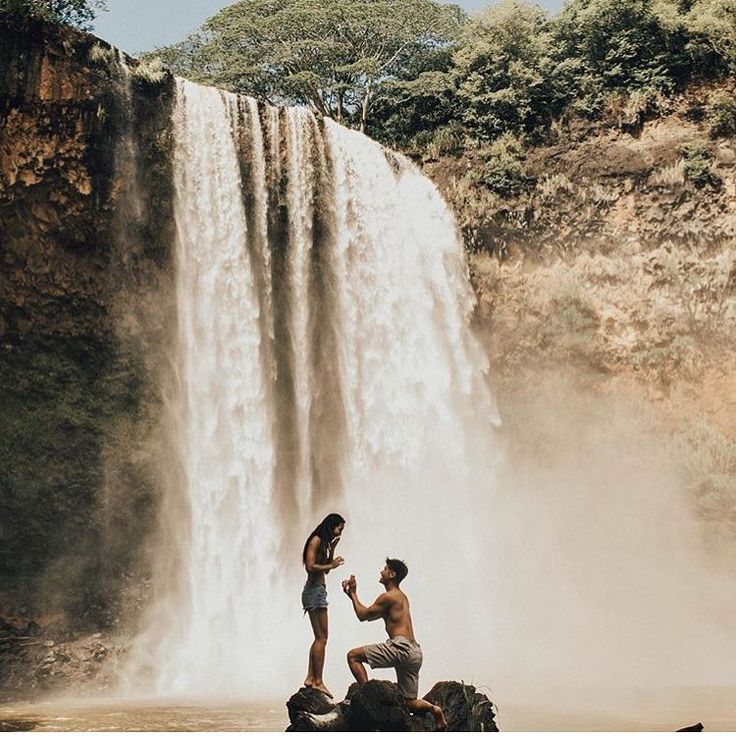 a man and woman standing in front of a waterfall with water pouring from the side