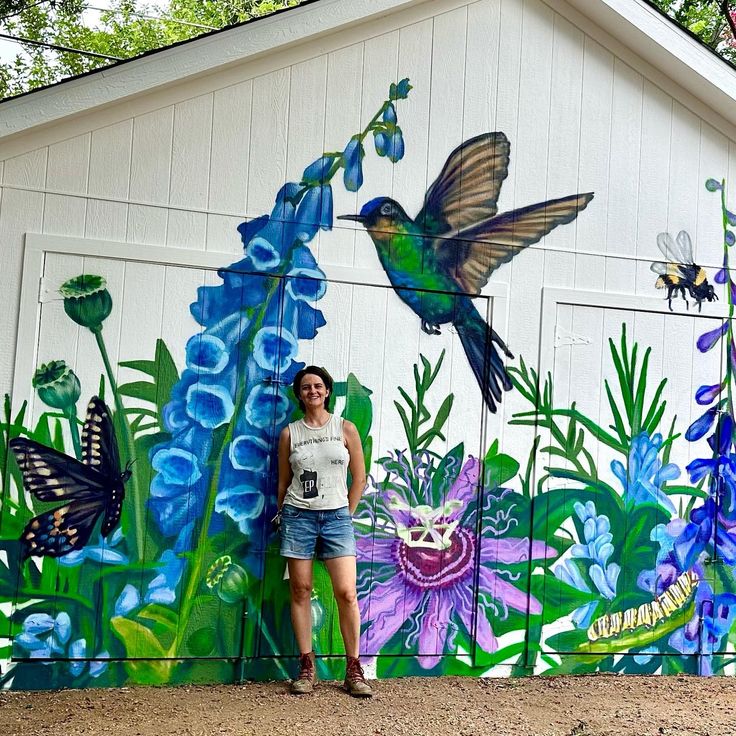 a woman standing in front of a painted mural on the side of a building with blue flowers