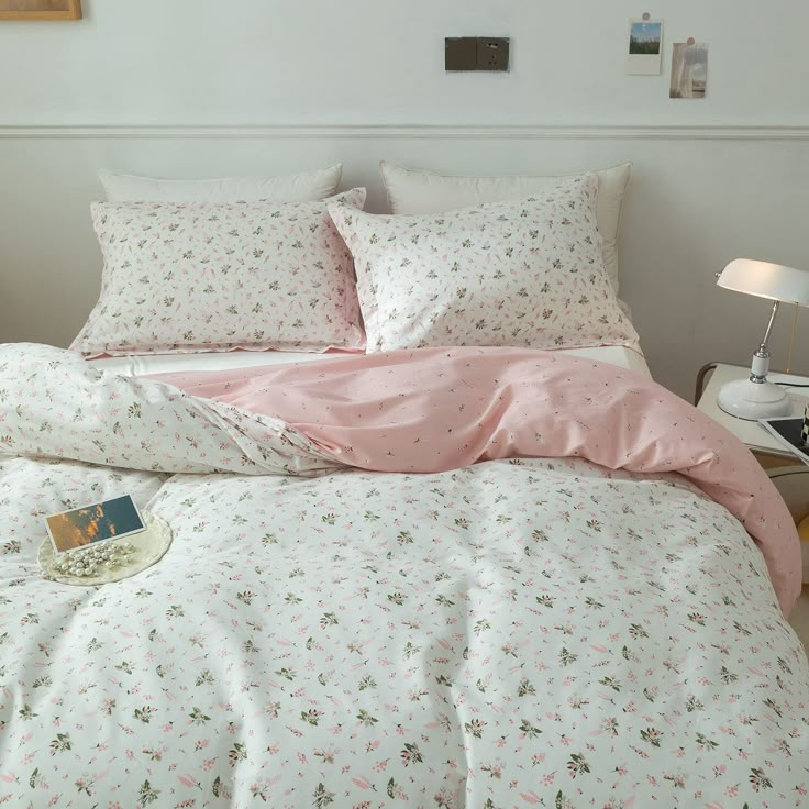 a bed with pink sheets and pillows in a bedroom next to a lamp on a table