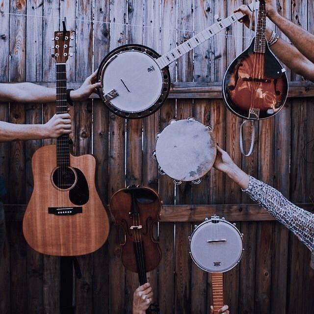 several people holding guitars and musical instruments in front of a wooden fence with strings hanging from it