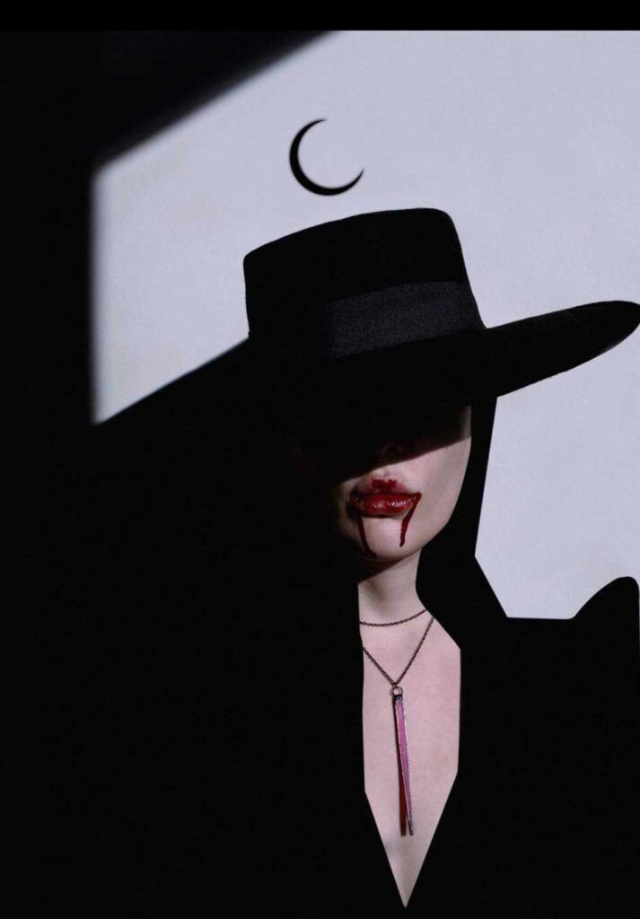 a woman wearing a black hat with red lipstick and a crescent moon on her face