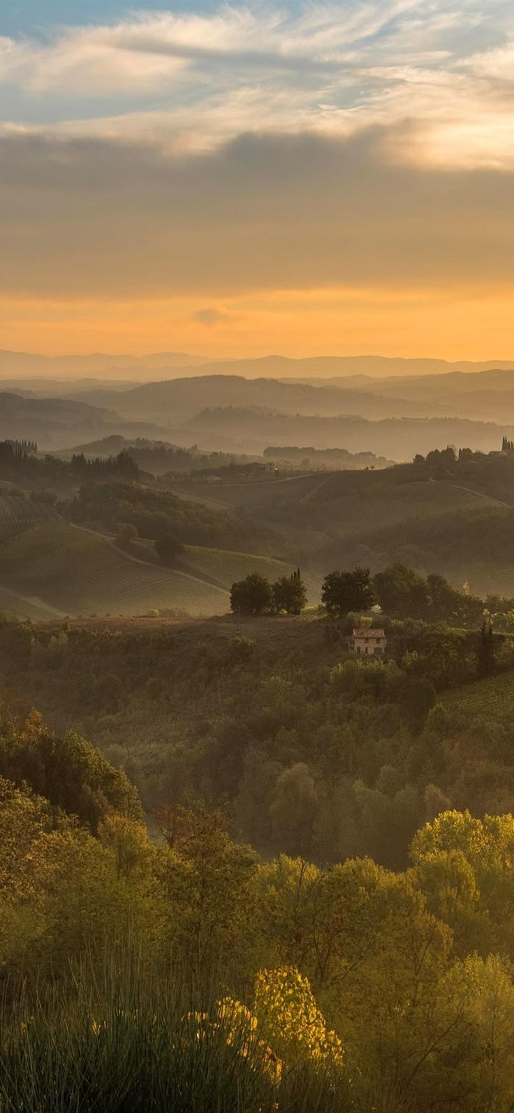 the sun is setting over rolling hills and trees in the foreground, with houses on the horizon