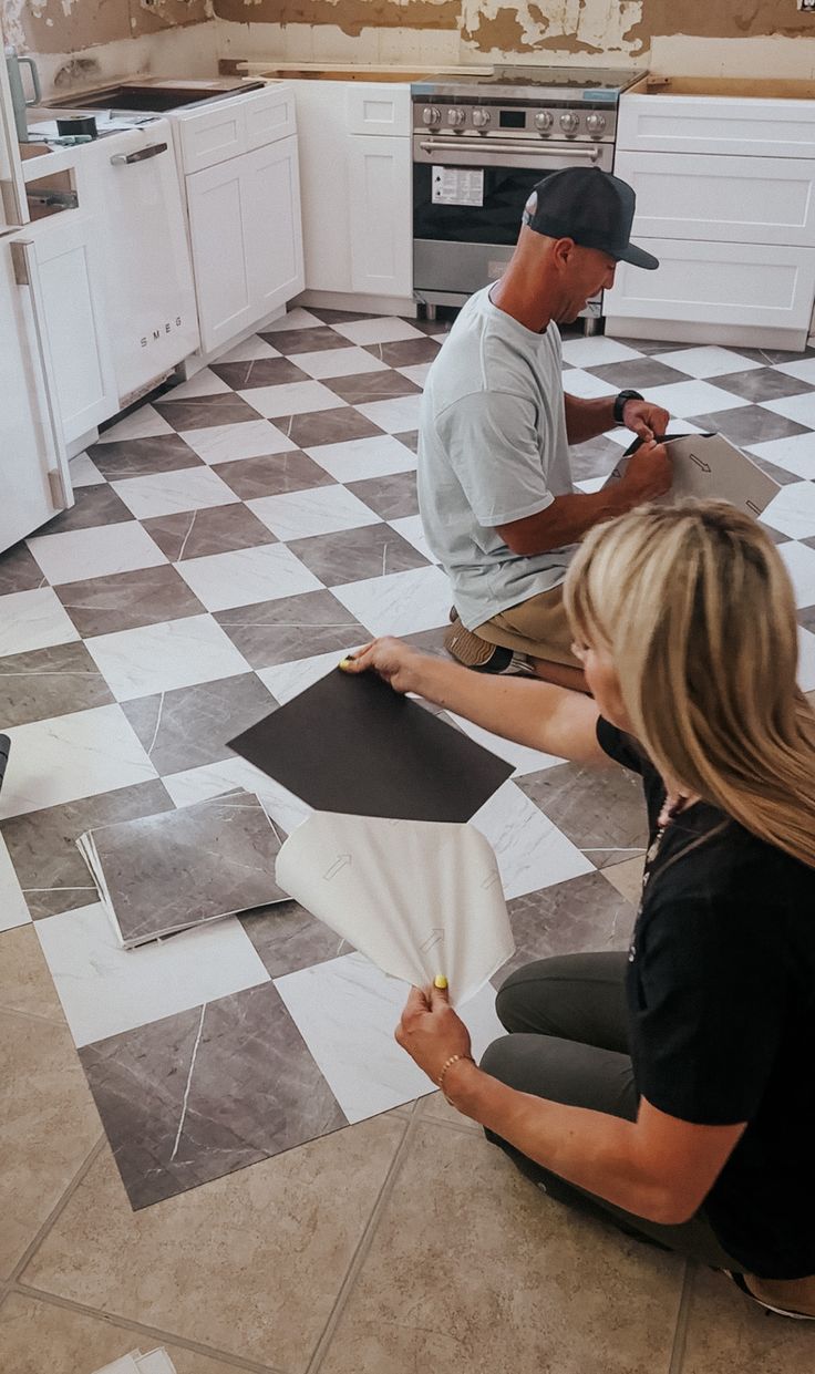 two people sitting on the floor in a kitchen working on some tile work with their hands