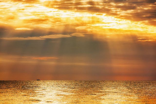 the sun is shining through clouds over the ocean with a small boat in the distance