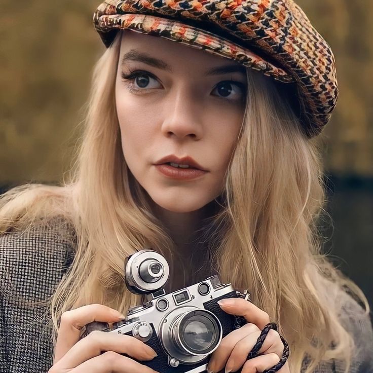 a woman holding an old fashioned camera in her hands and wearing a hat on top of her head