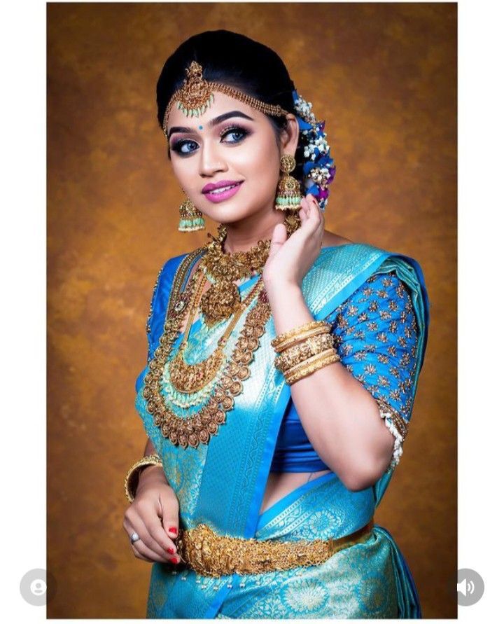 a woman in a blue and gold sari with jewelry on her head, posing for the