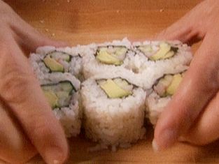 two hands reaching for sushi on a wooden table