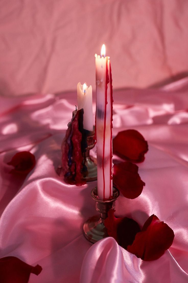 two candles sitting on top of a table covered in pink fabric and rose petal