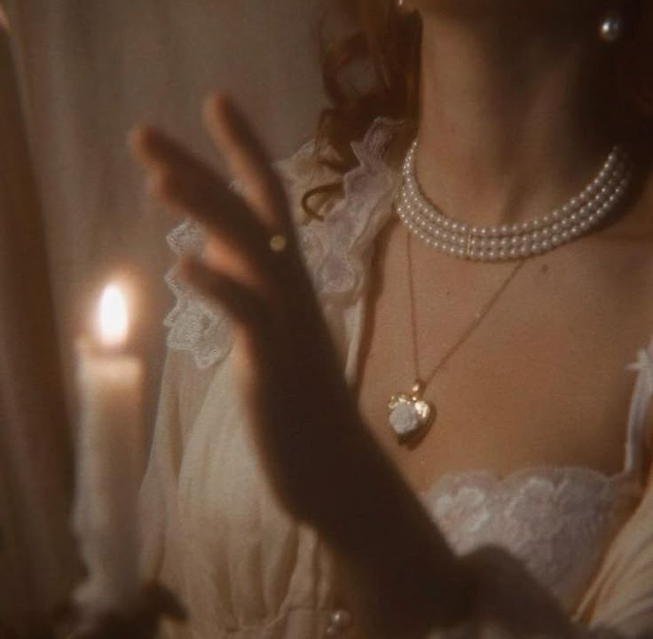 a woman in a white dress is holding her hand out to the side while wearing pearls and necklaces