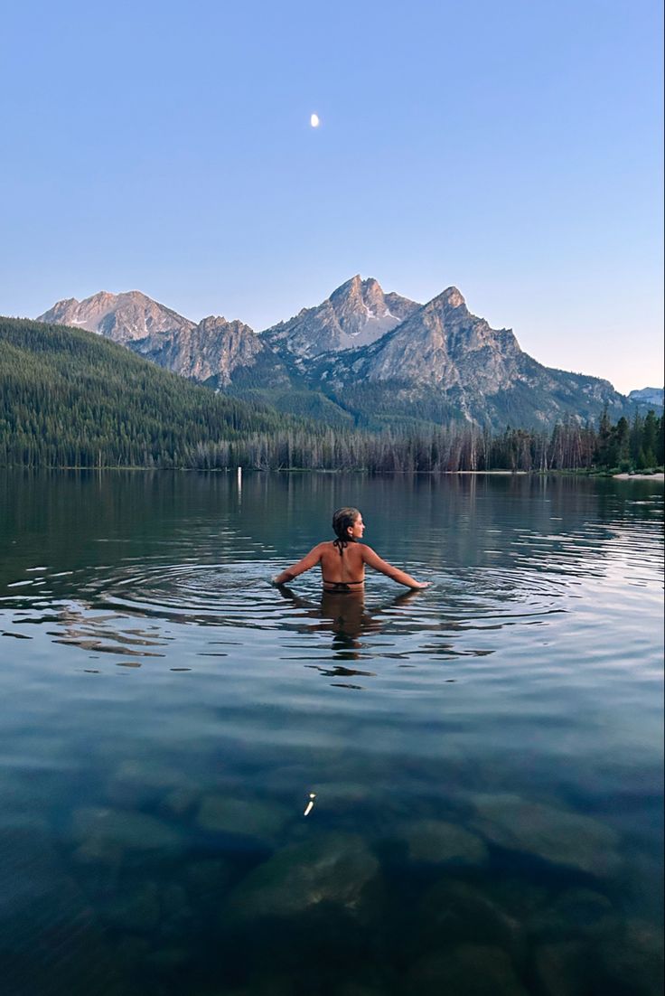 a woman in a body of water with mountains in the background and a half moon above her head