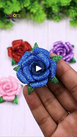 a hand holding a small blue flower in front of some pink and purple flowers with green leaves