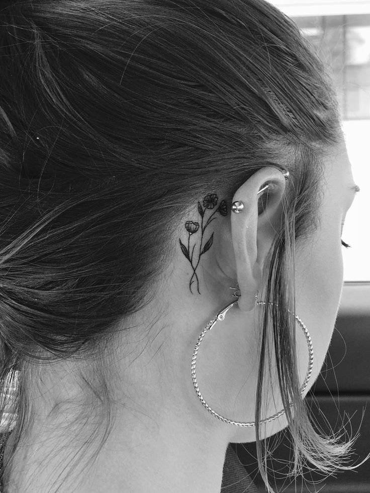 a woman with a flower tattoo on her left ear and behind the ear is a pair of hoop earrings