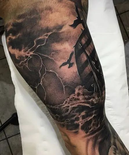 a man's arm with a ship on it and birds flying in the sky