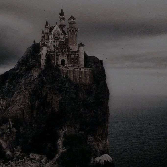 a castle sitting on top of a cliff next to the ocean under a cloudy sky