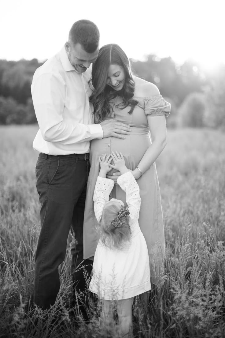 a pregnant woman and her husband standing in tall grass with their hands on the belly