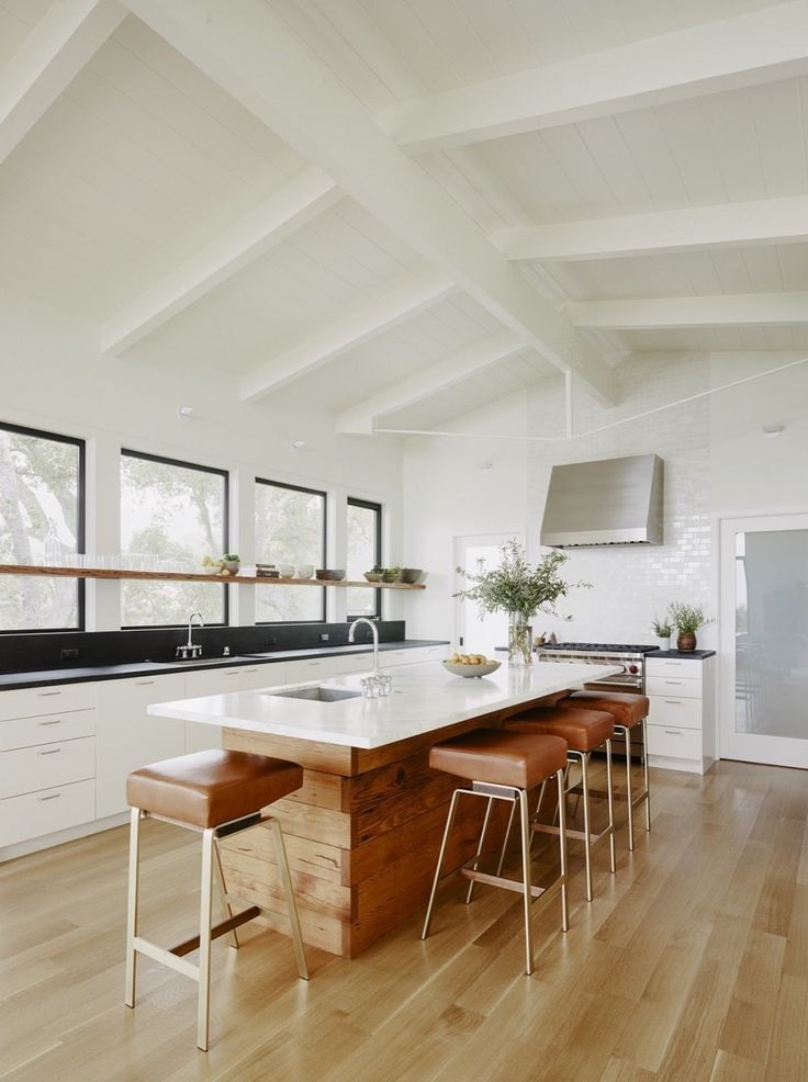 a kitchen with white walls and wooden flooring has an island countertop that seats four stools