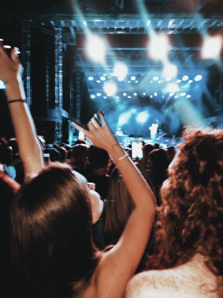 a crowd of people at a concert with their hands in the air and lights on