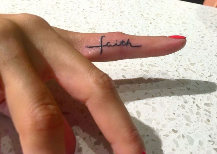 a woman's finger with the word faith tattooed on her left thumb and red nail polish