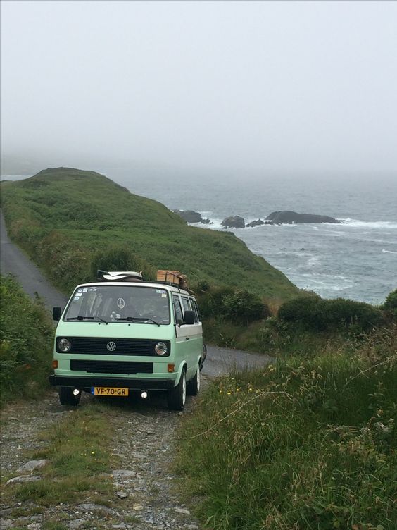 a green van parked on the side of a road next to the ocean and grass