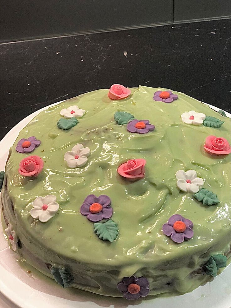 a green cake with flowers on it sitting on a white plate in front of a black counter