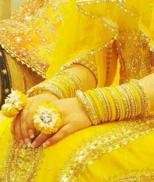 a woman in yellow dress holding flowers and wearing gold bracelets with her hands on her chest