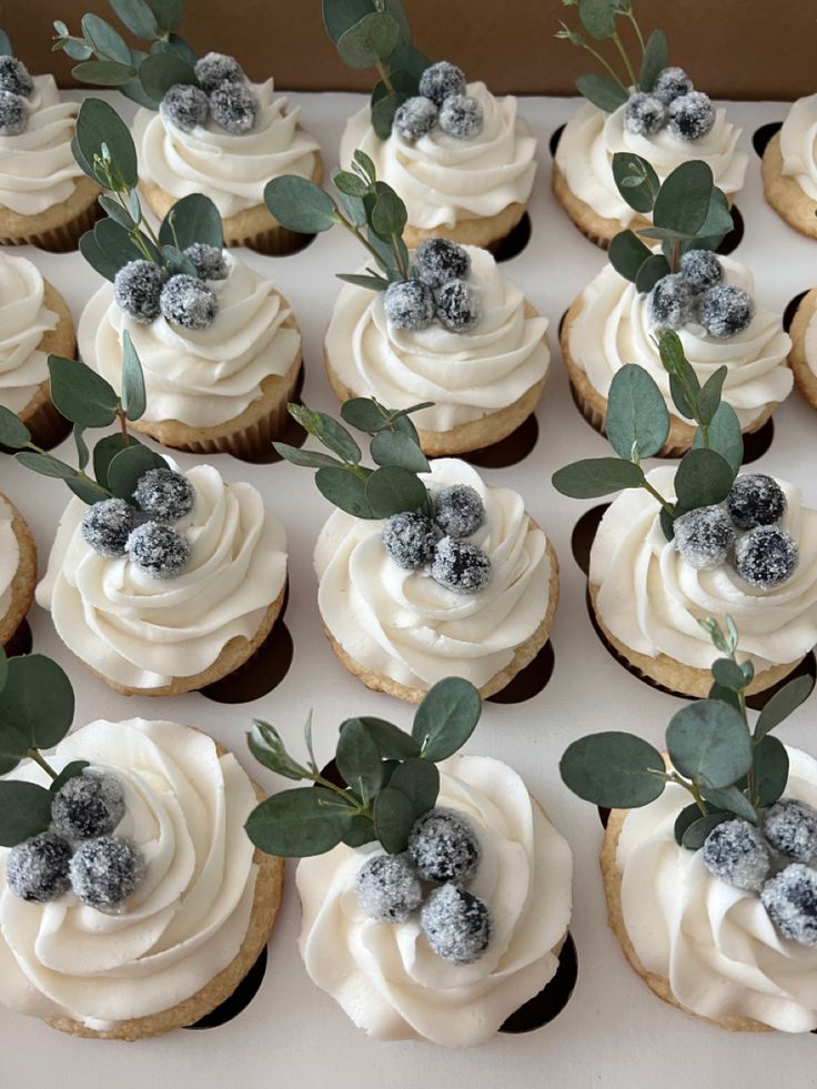 there are many cupcakes with frosting and berries on top that are decorated with green leaves