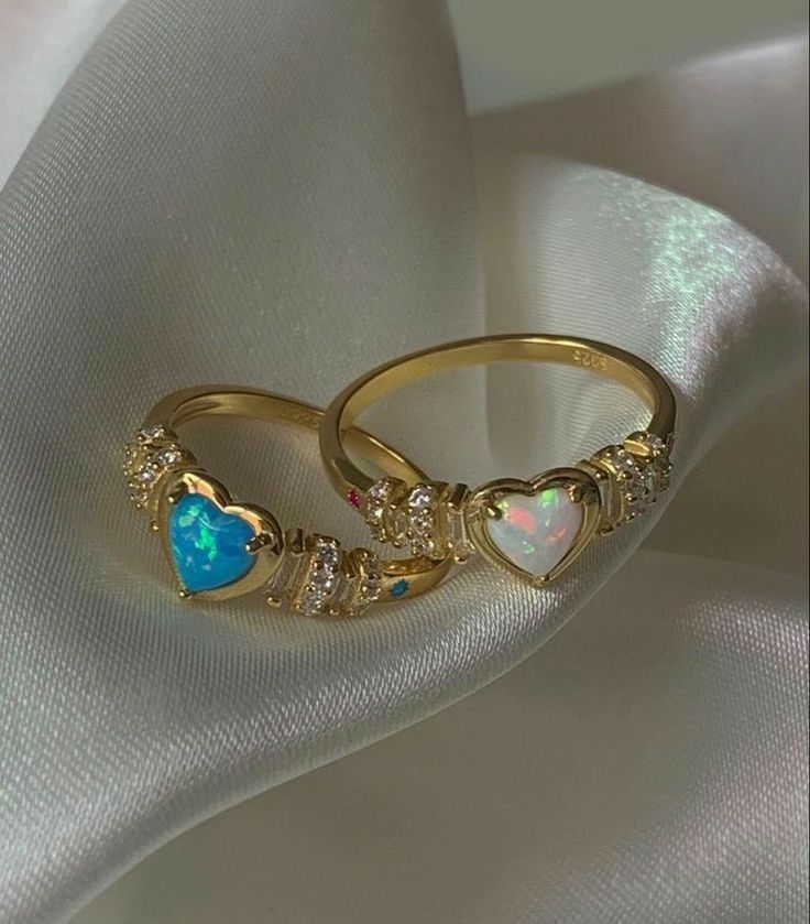 two gold rings with opal and diamond accents on white satin background, closeup