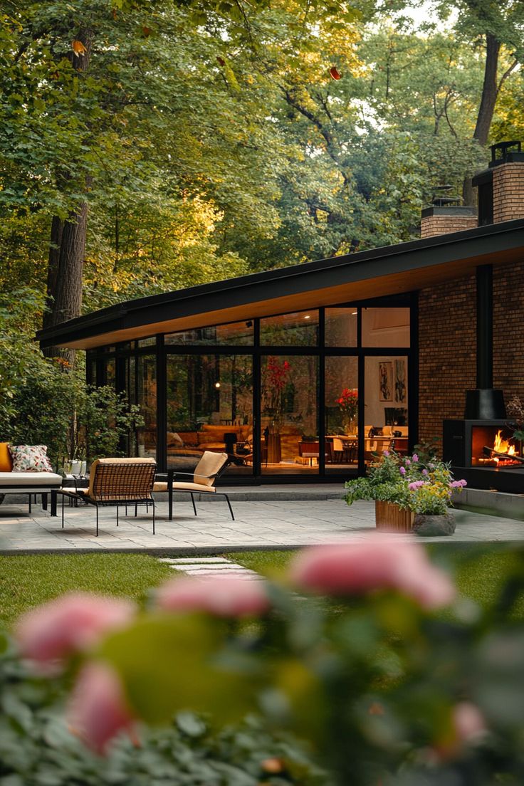 a modern house in the woods surrounded by greenery and pink flowers with an open fire place