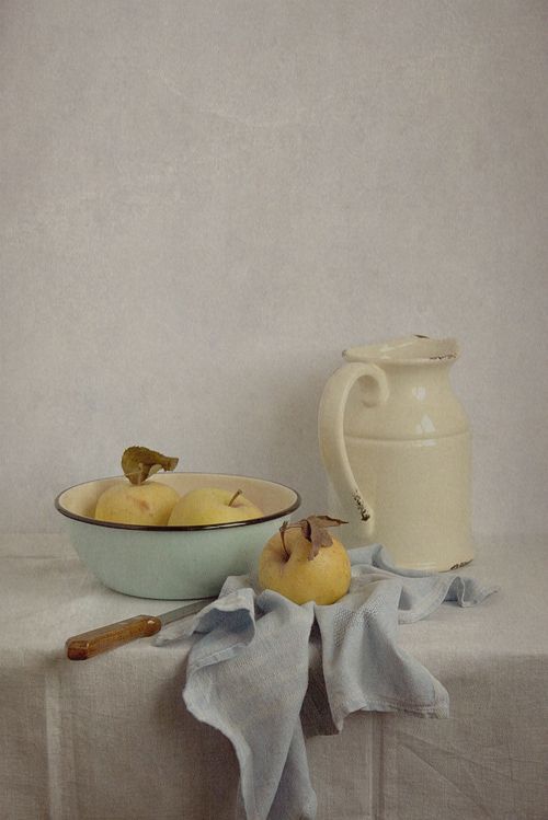 a painting of apples in a bowl next to a pitcher and cloth on a table