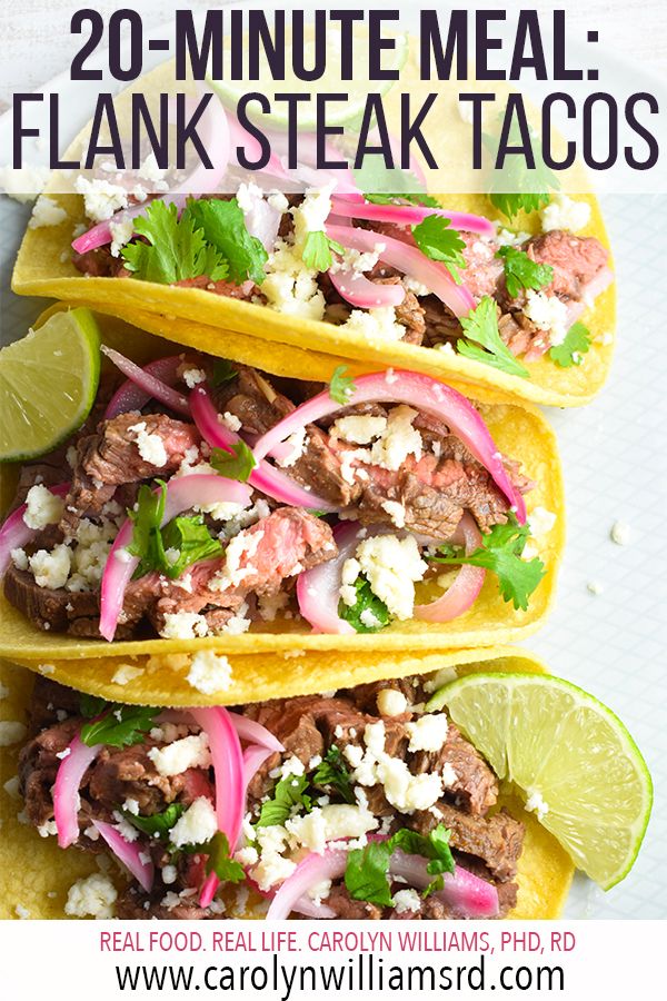 two steak tacos with onions, cilantro and lime wedges on top