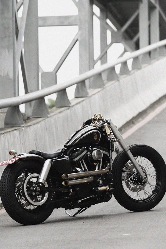 a black and white photo of a motorcycle parked on the side of a road next to a bridge