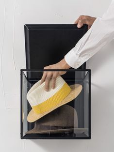 a person is holding a hat in a clear box on the wall with white walls