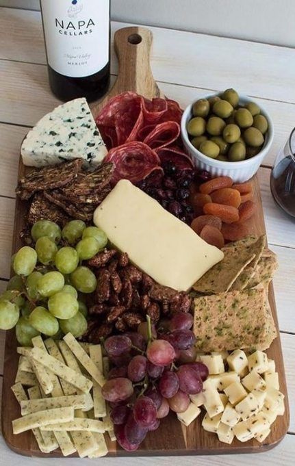 an assortment of cheeses, crackers and grapes on a wooden platter