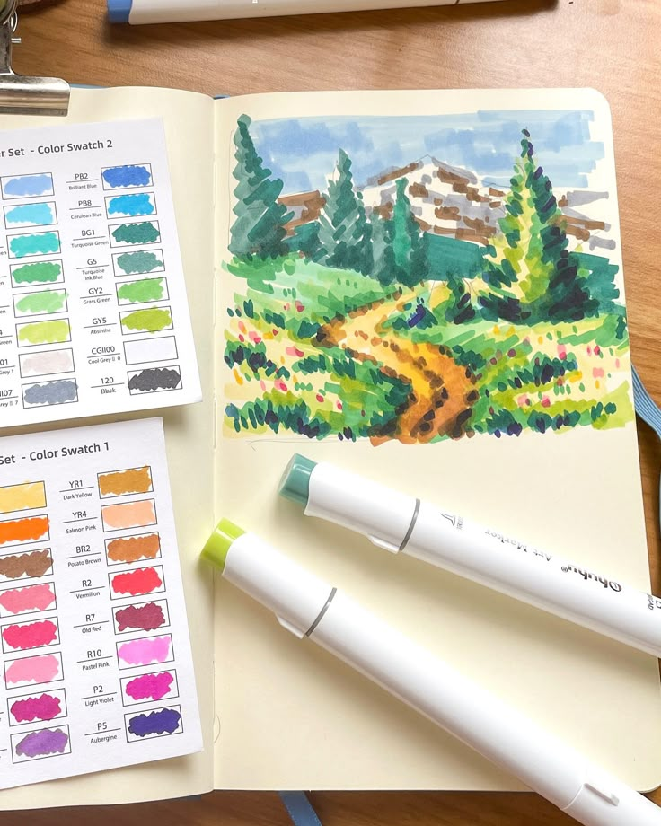 three watercolors are sitting on top of an open book with markers and pens